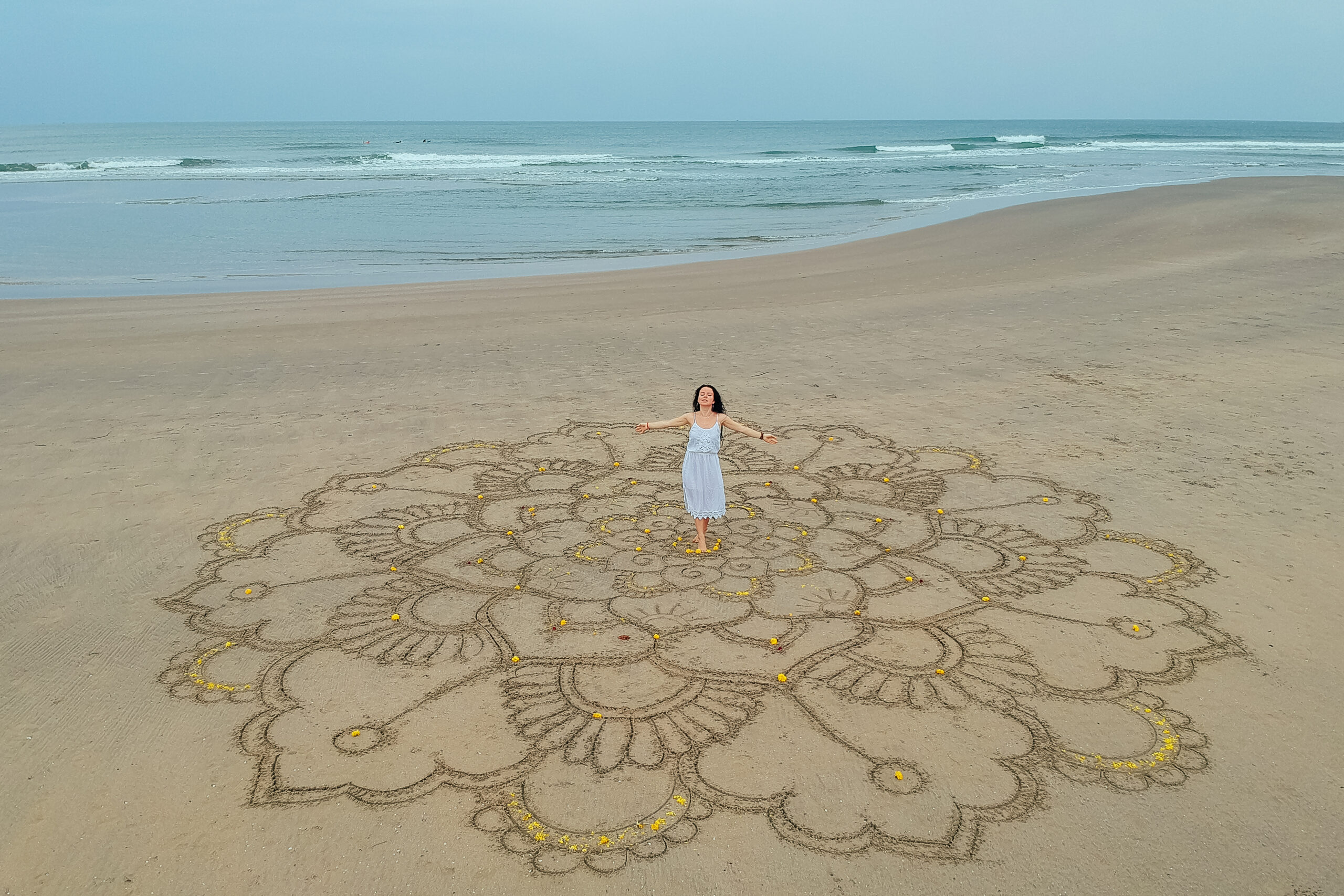 a large mandala painted on the sand on the ocean with a girl in the middle boho style. Fernheilung Modul Psyche